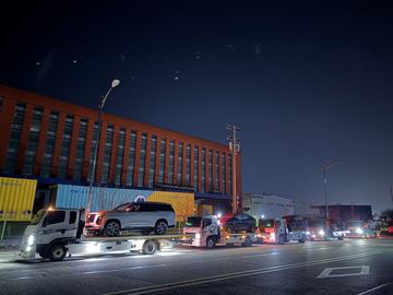 야간 도로변에서 대형 SUV를 실은 카캐리어와 뒤이은 차량들