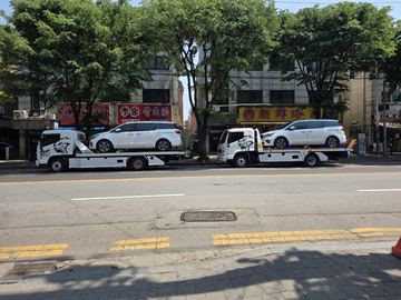 도심 도로에서 카캐리어 두 대가 흰색 승합차를 각각 한 대씩 싣고 서 있는 모습